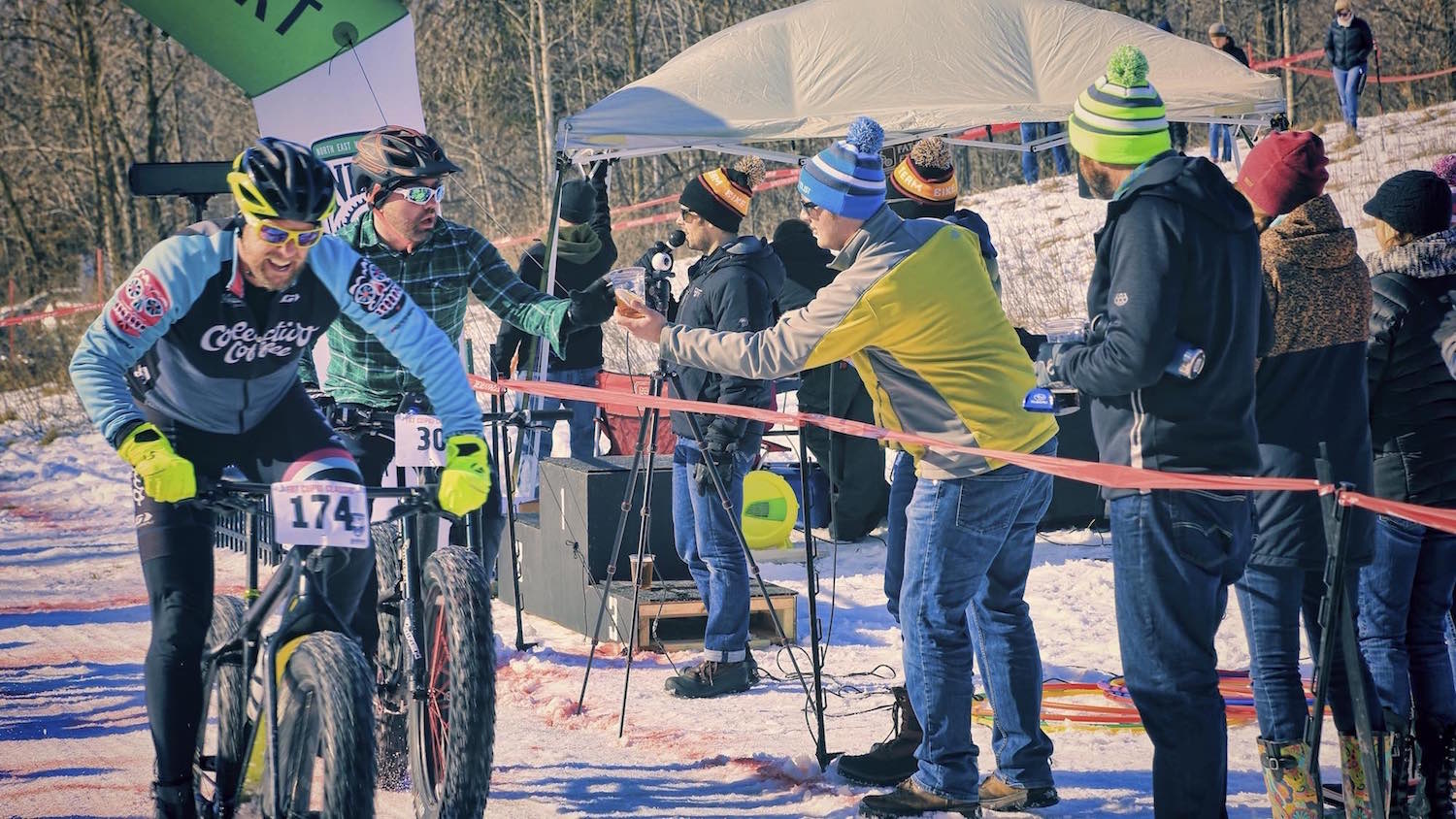 Matt Fisher from Recyclist Bicycle Company hands a beer to a  fat bike racer during the Fat Cupid Classic.